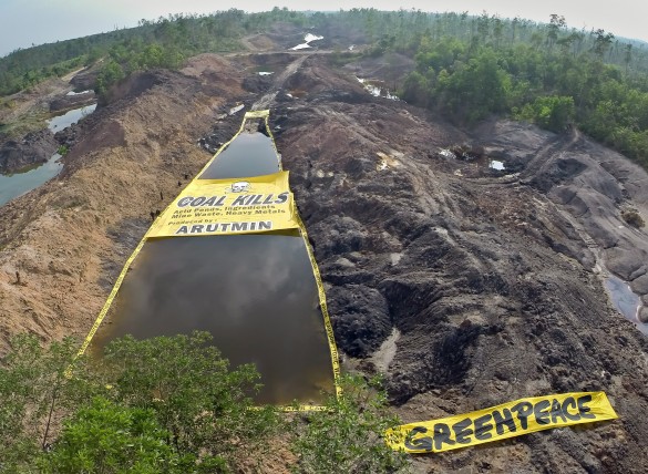 Greenpeace activists unfurl a banner reading “Coal Kills. Acid Ponds Ingredients: Mine Waste, Heavy Metals Produced by: Arutmin”, at the Asam-asam Coal Mine in South Kalimantan, which is scarred with toxic settling ponds used by the coal industry. The activists also surround the pond with 'Caution: Toxic Water' tape. Greenpeace is calling on the provincial and national government to stop the coal industry poisoning the water sources and local environment that communities rely on.